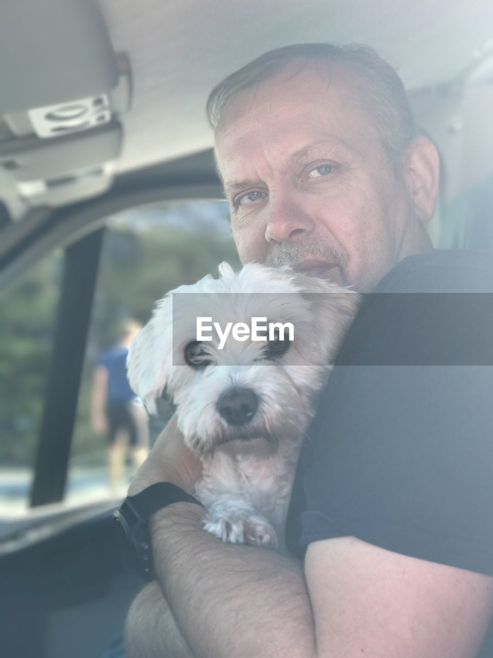 Man embracing dog while sitting in car