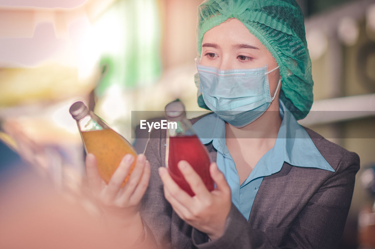 Close-up of woman wearing mask inspecting drinks in factory