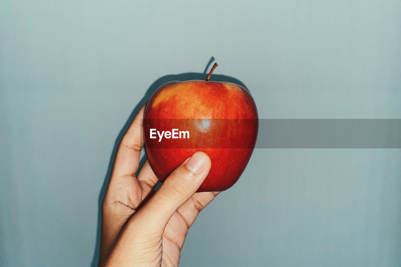 Close-up of hand holding apple against white background