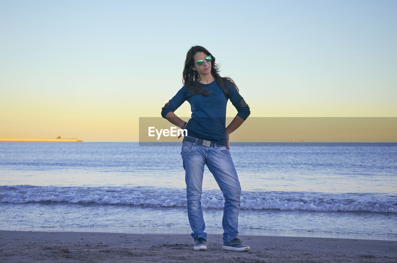 Full length of woman standing at beach against clear sky during sunset