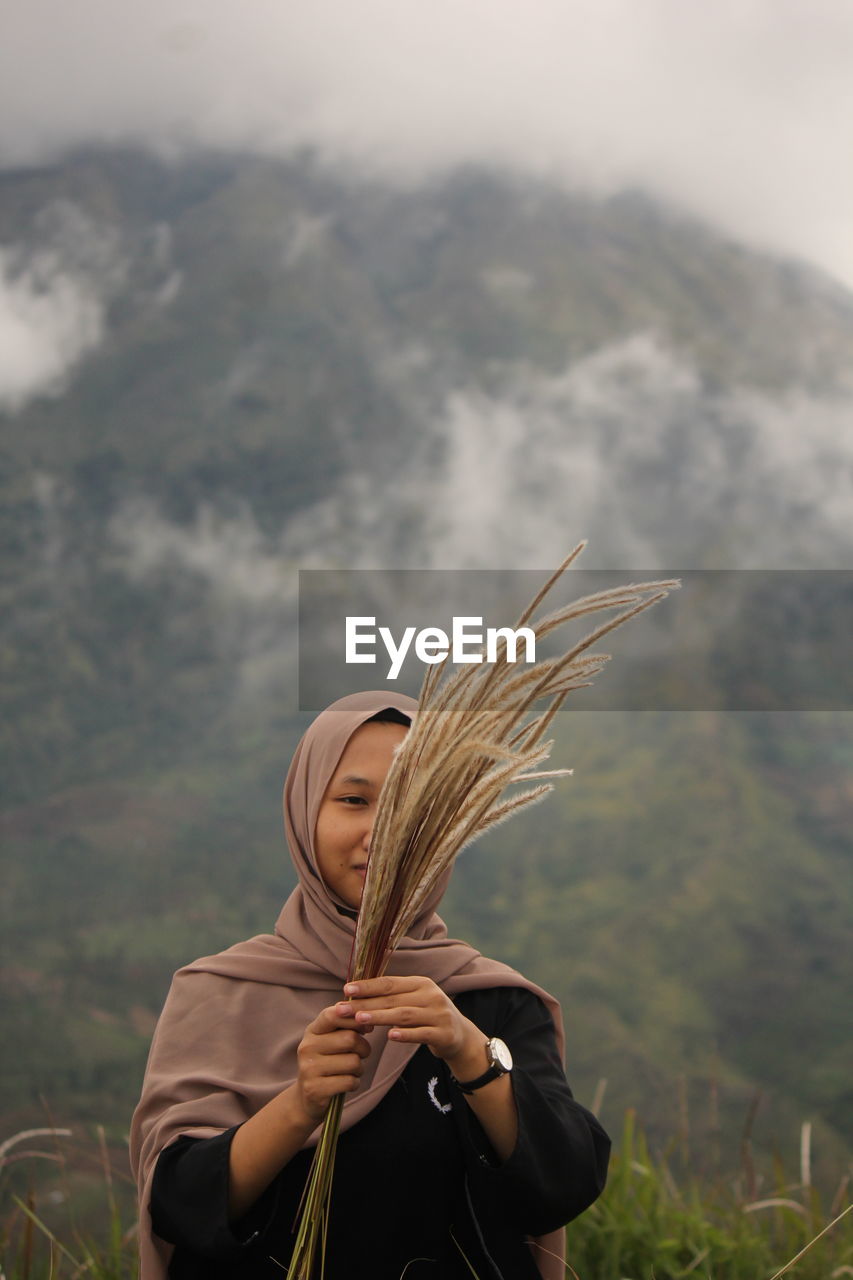 Woman holding plants while standing against mountain