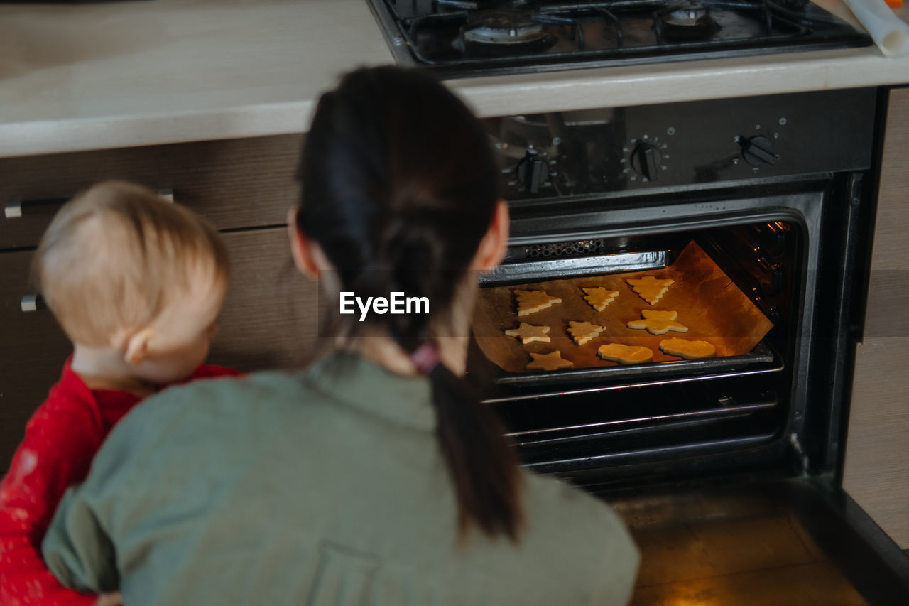 Family, mom with toddler baby girl cooking gingerbread and puts cookies in oven. christmas homemade