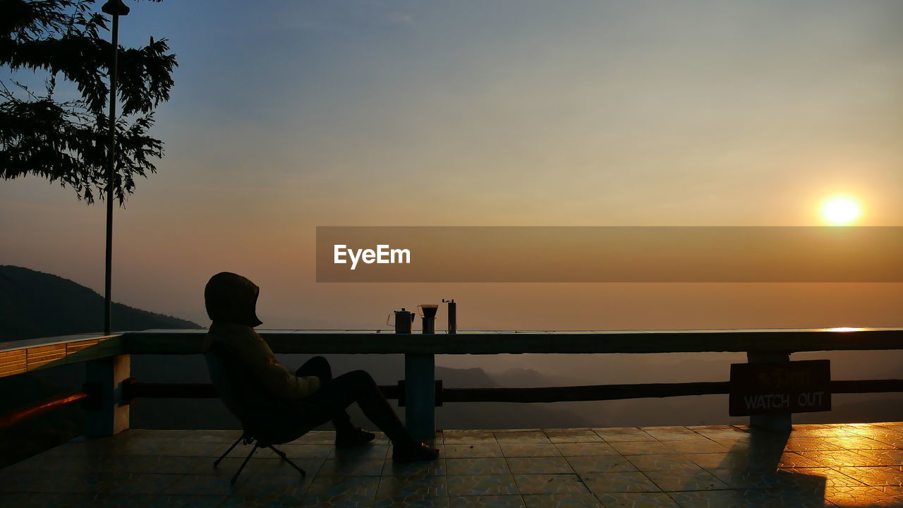 SILHOUETTE MAN SITTING ON SWIMMING POOL AT SUNSET