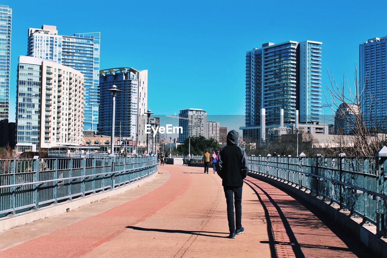 FULL LENGTH REAR VIEW OF MAN WALKING ON CITY