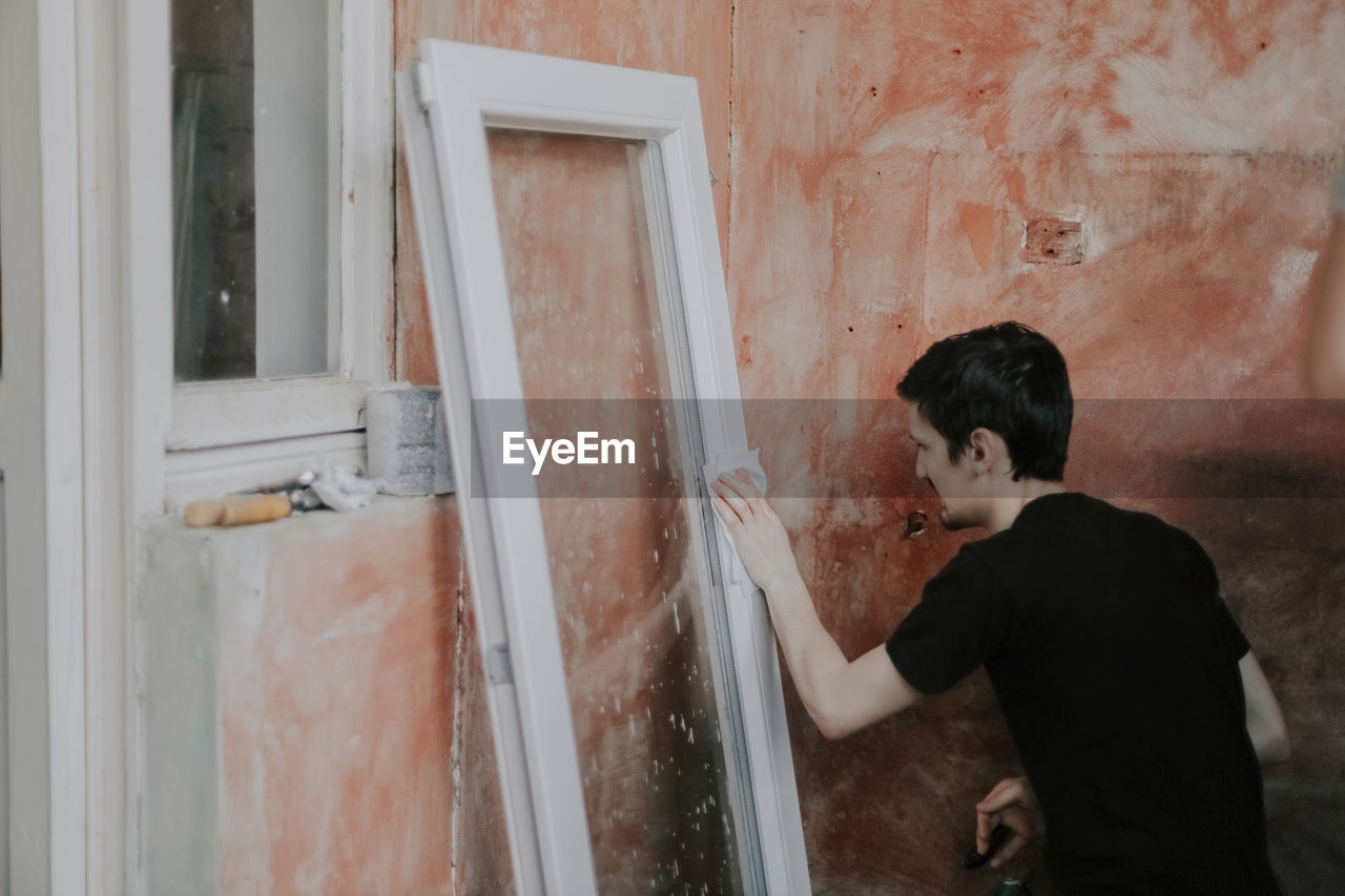 Caucasian young man wipes a window frame with a dry paper napkin.