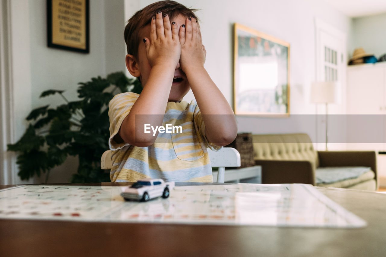 Toddler sitting at table playing peekaboo and covering his eyes