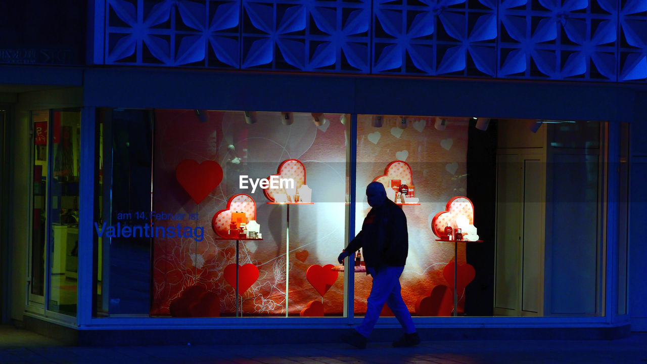 FULL LENGTH OF WOMAN STANDING BY ILLUMINATED BUILDING