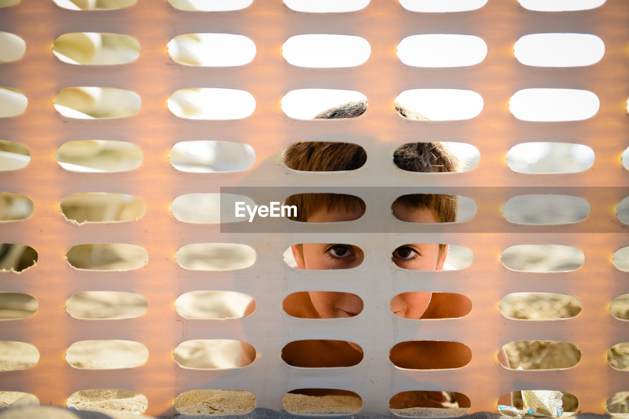 Portrait of boy seen through metal grate at beach