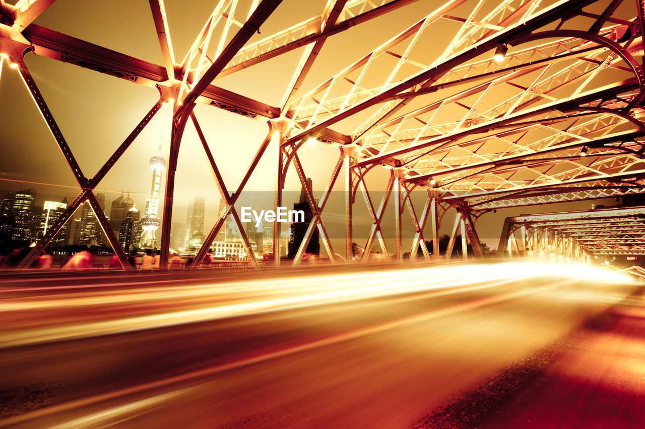 LIGHT TRAILS ON BRIDGE IN CITY AGAINST SKY