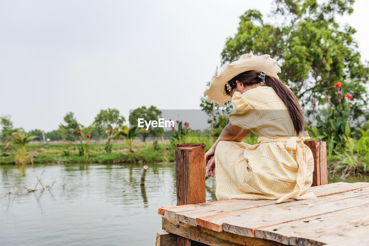 Woman sitting on wood by lake against trees