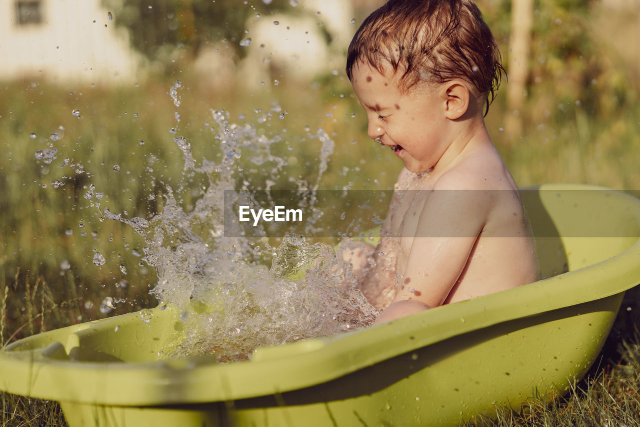 Cute little boy bathing in tub outdoors in garden. happy child is splashing, playing with water