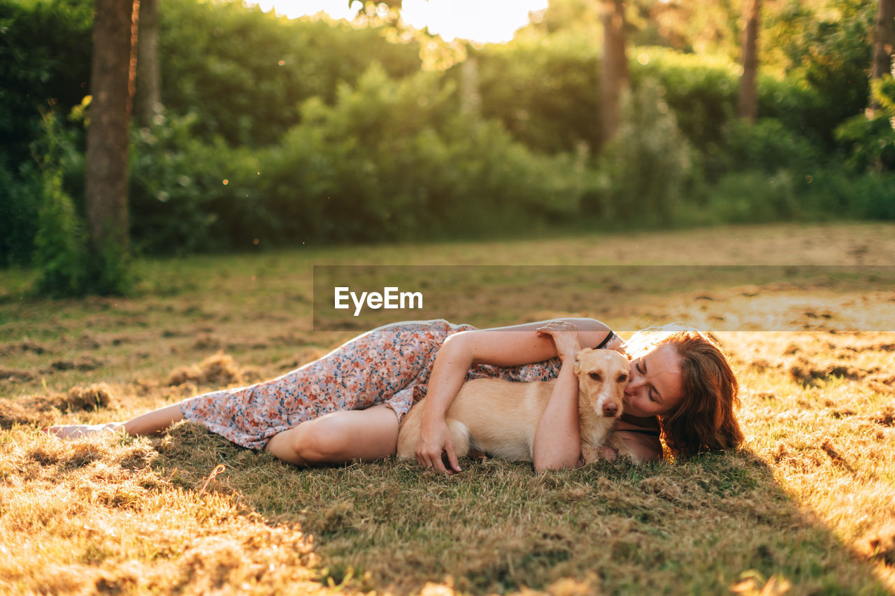 Woman lying on the grass embraces and cuddles her dog in the light of the sunset in a bucolic scene