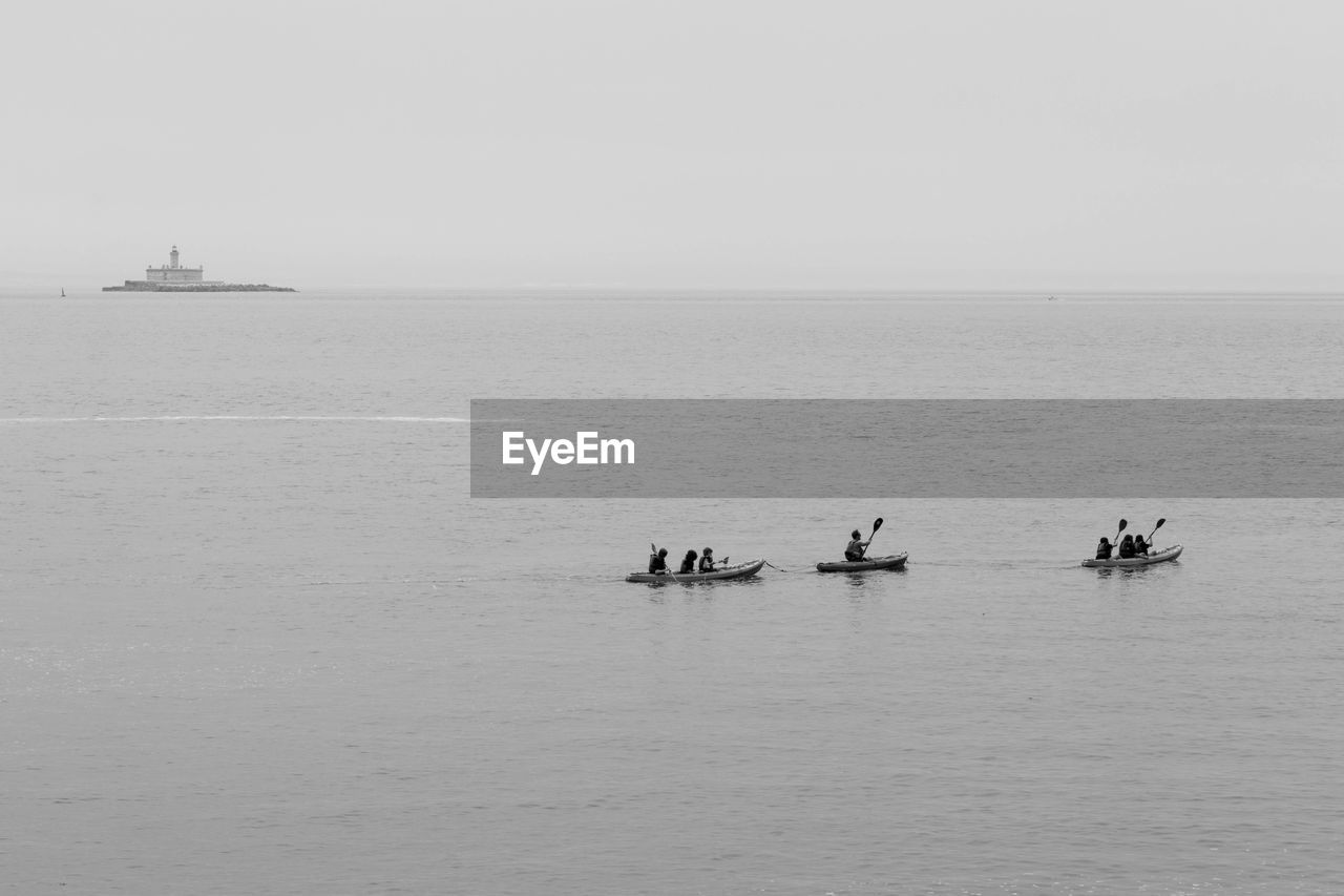 Distant view of people canoeing on sea against sky