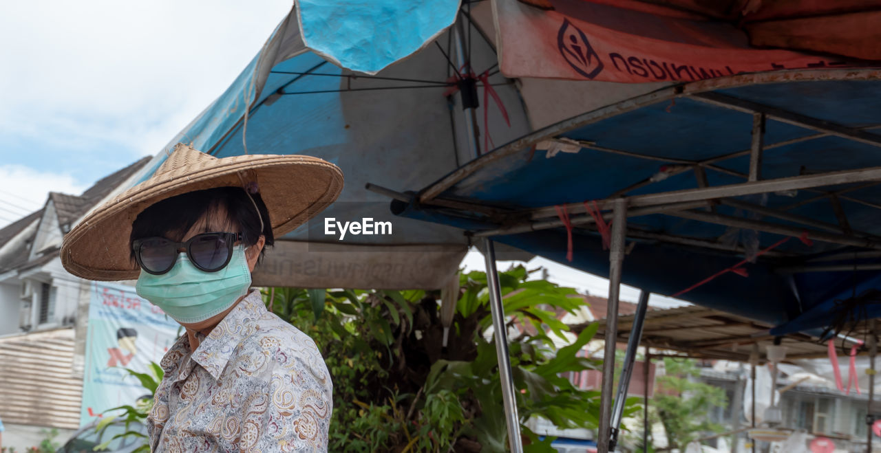 PORTRAIT OF WOMAN WEARING SUNGLASSES STANDING BY TRADITIONAL WINDMILL