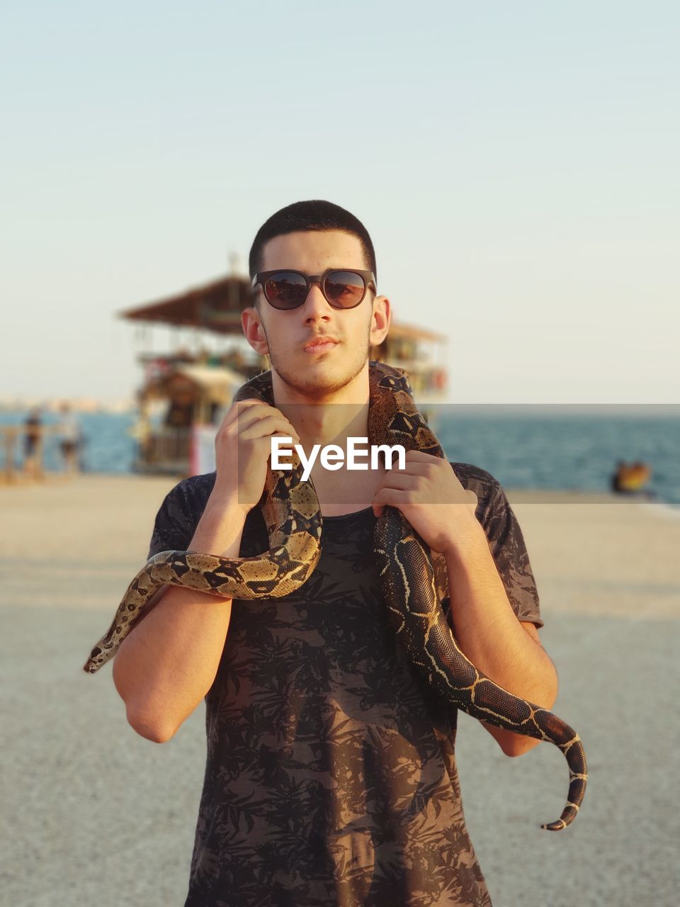 Portrait of young woman with snake wearing sunglasses standing at beach