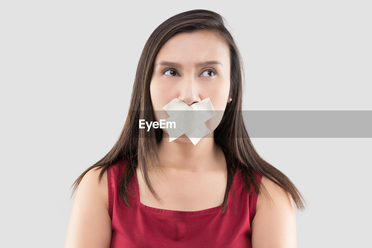 Woman looking away with bandage on mouth against white background