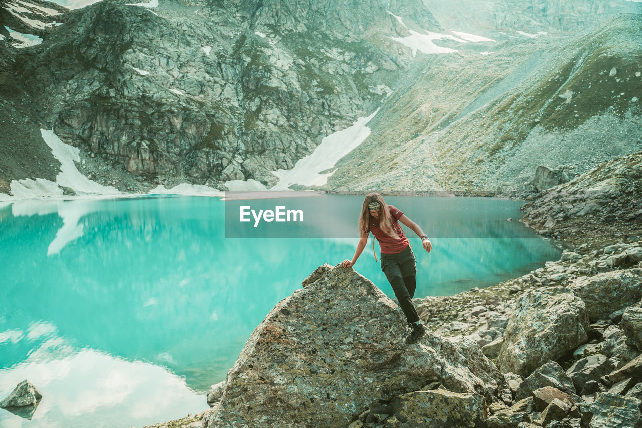 YOUNG WOMAN STANDING ON ROCK BY WATER