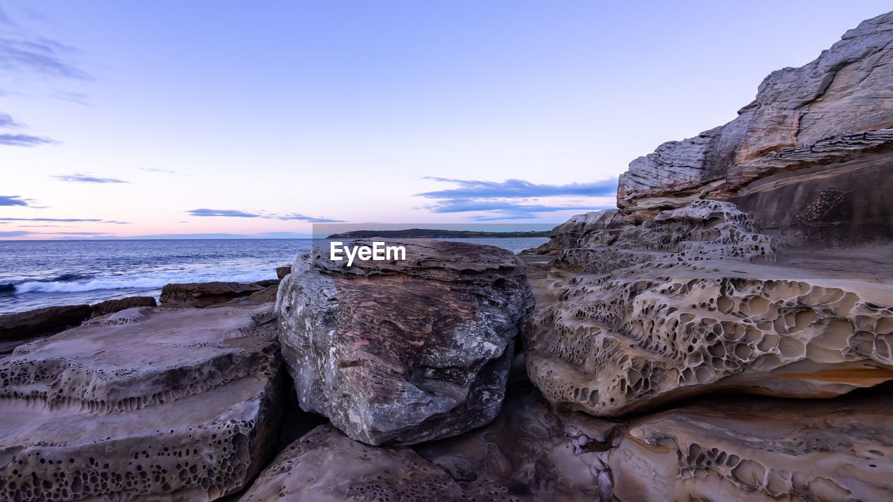 Rocks on beach against sky during sunset