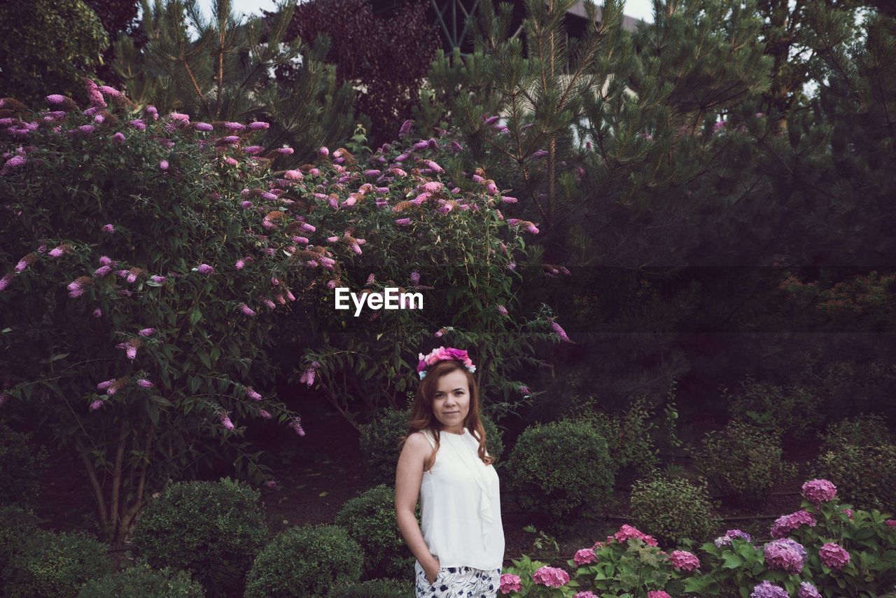 Portrait of young woman standing amidst plants at park