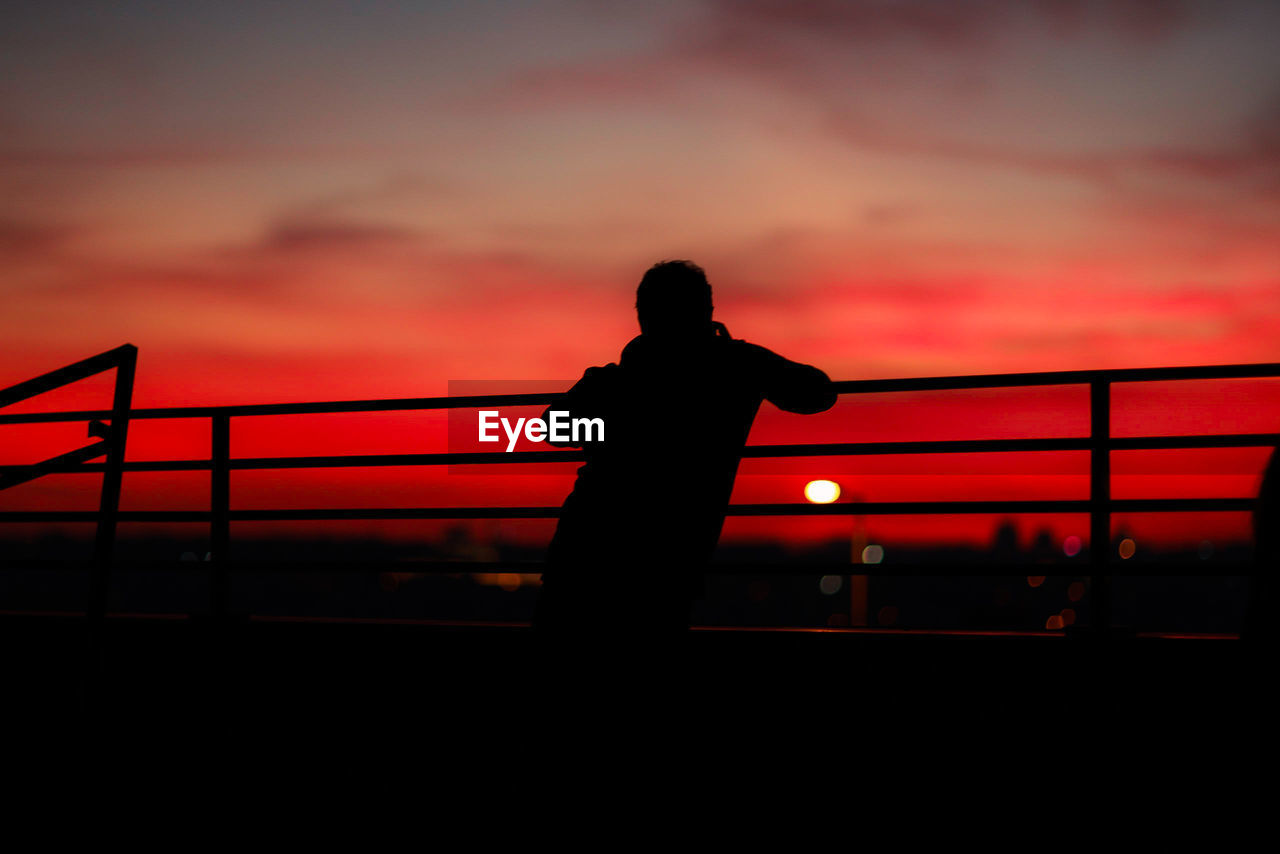 Silhouette of man standing by railing against sky during sunset