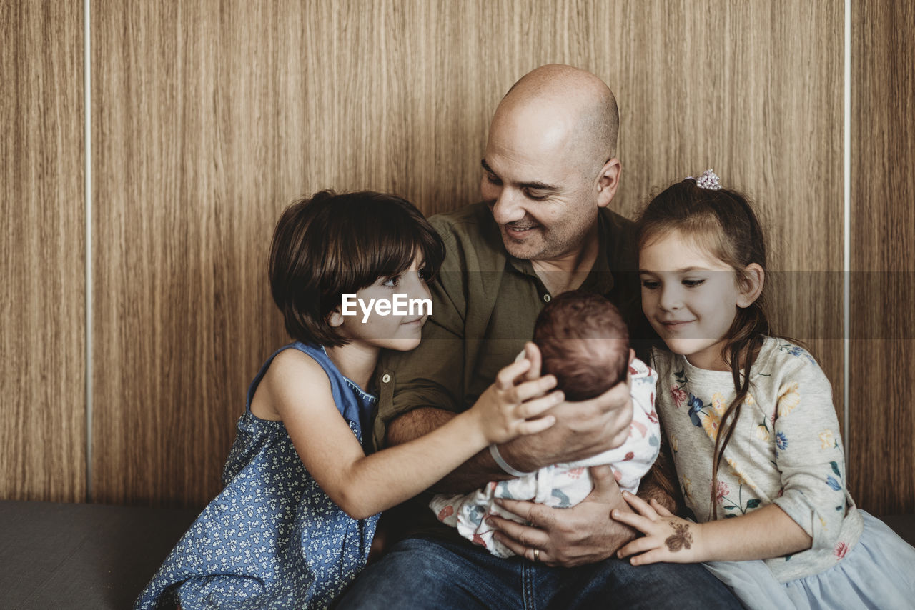 Front view of father holding newborn son with siblings