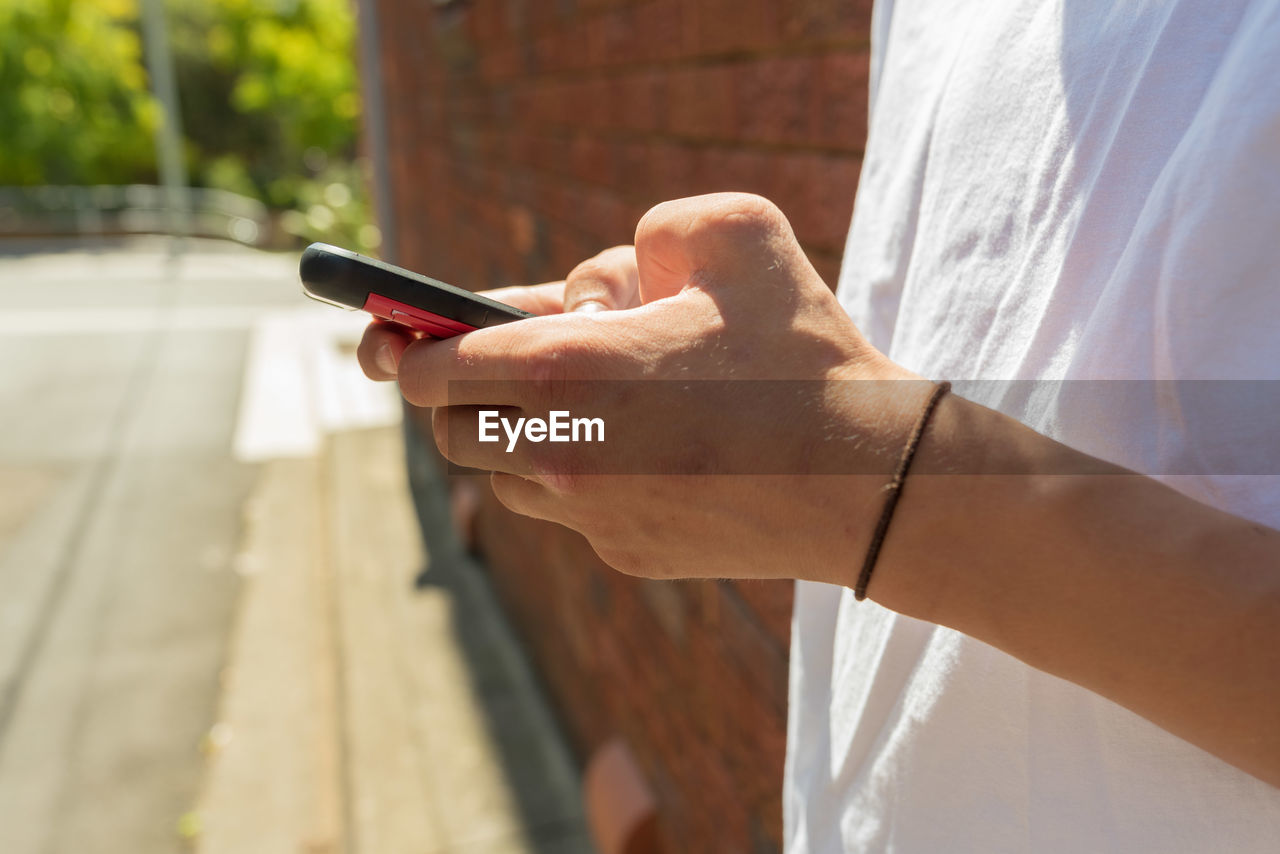 Midsection of teenage boy using phone against brick wall