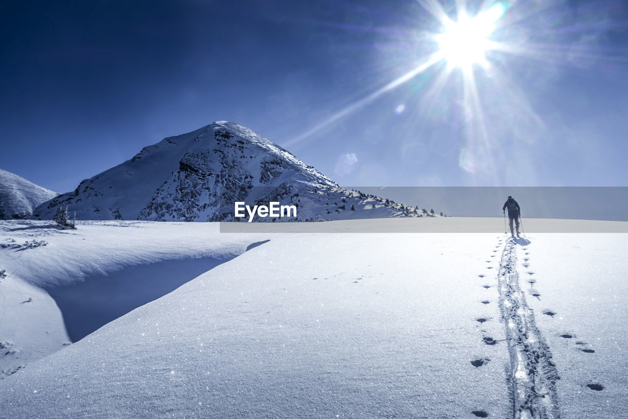 Rear view of man hiking on snow against sky