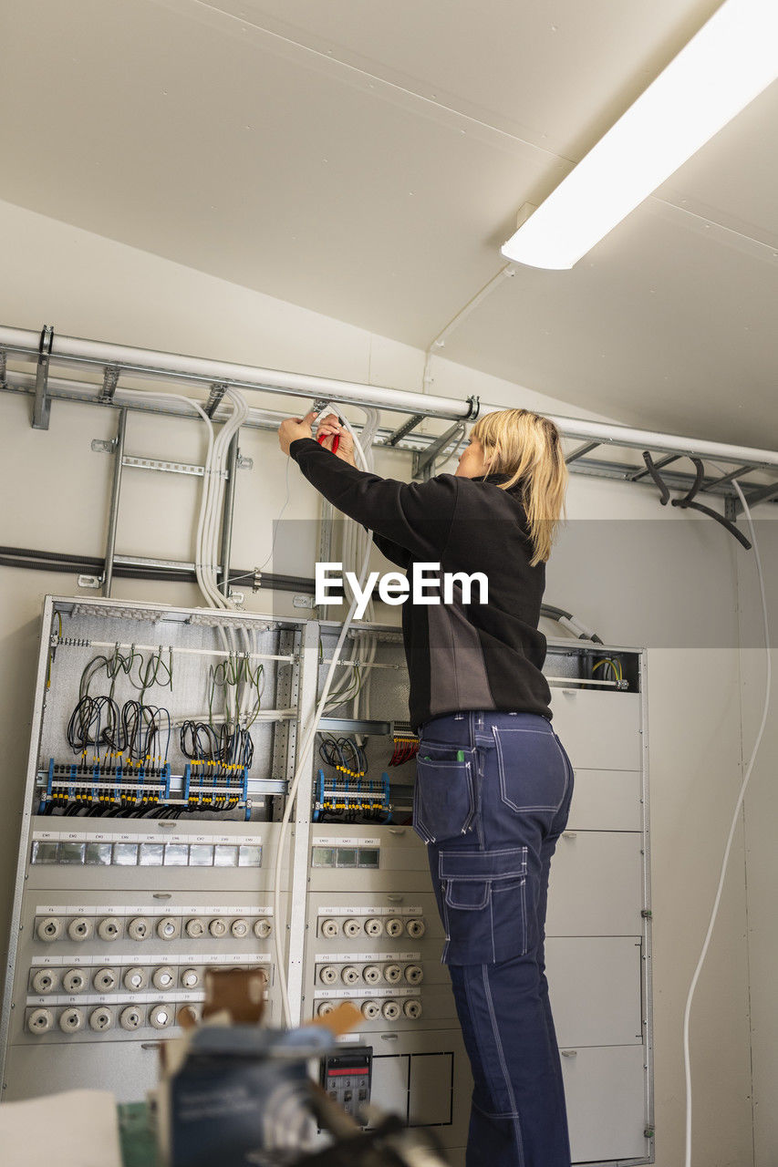 Female technician installing cables by meter board in industry