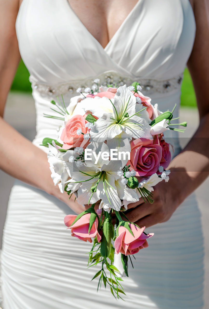 Midsection of bride holding bouquet outdoors