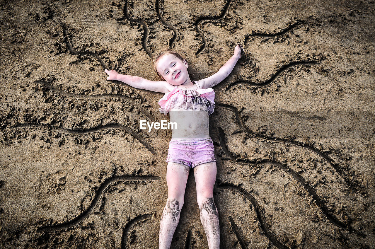 High angle portrait of happy girl lying on sand at beach