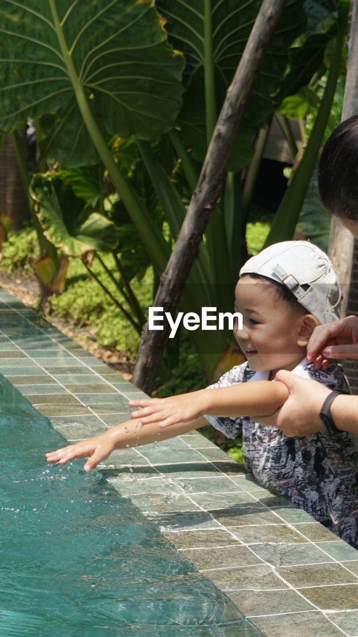 Cropped hands of mother holding cute son standing by swimming pool