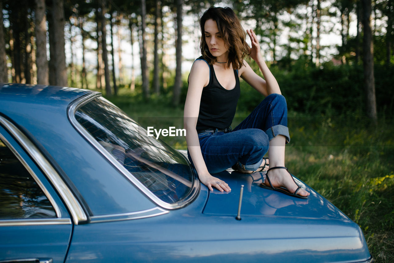 Young hipster woman sitting on a blue vintage car.