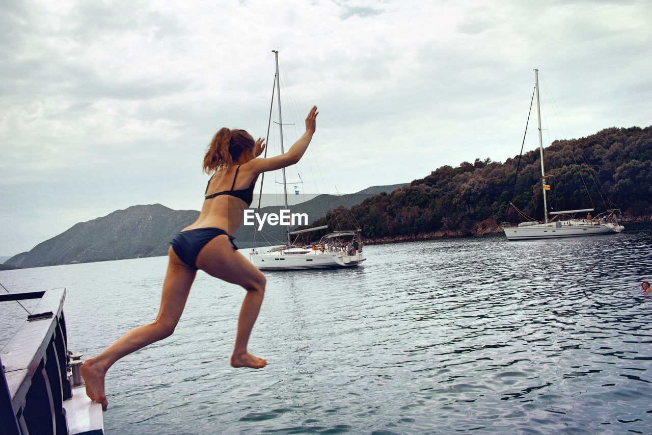 Full length of woman jumping in sea against sky