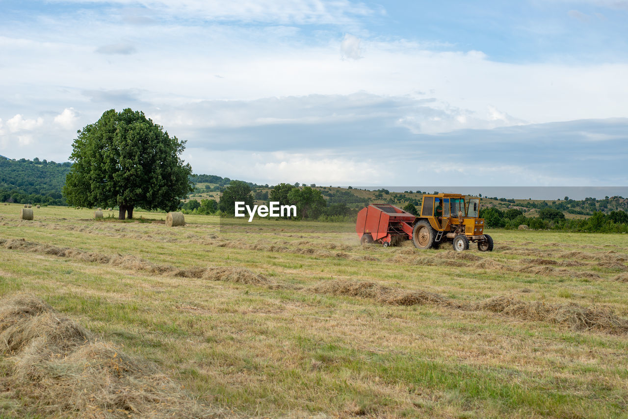 Tractor with bailing trailer working on the field gathering grass for gay bales