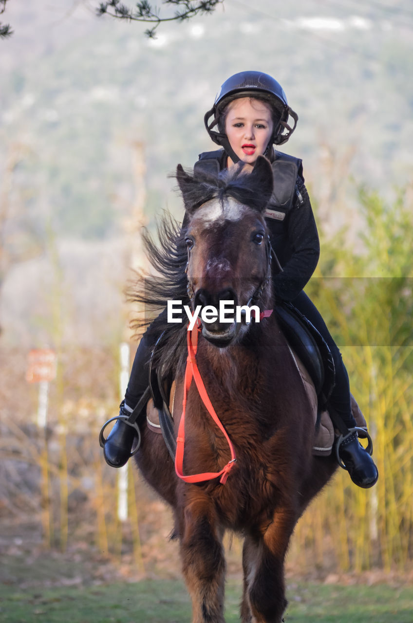 PORTRAIT OF TEENAGE GIRL RIDING HORSE ON FIELD