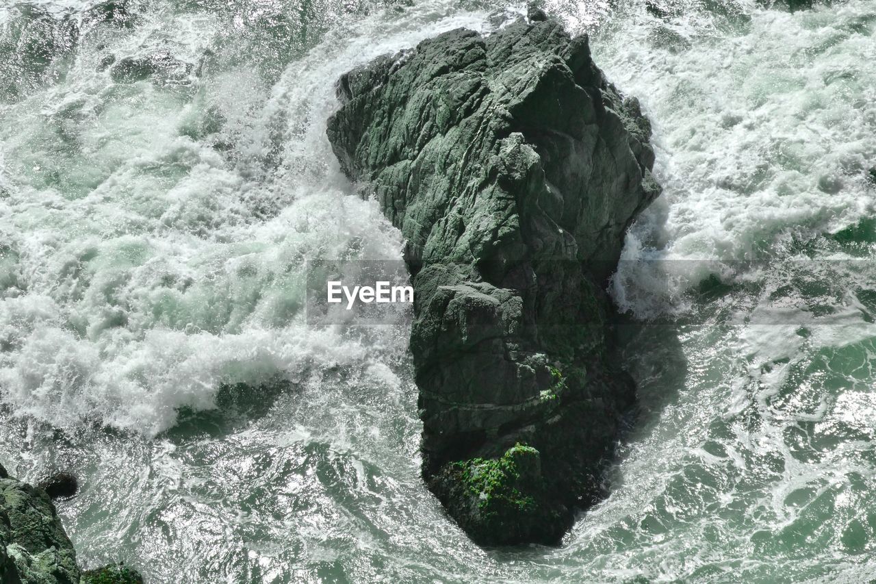 HIGH ANGLE VIEW OF WATER FLOWING THROUGH ROCKS IN SEA