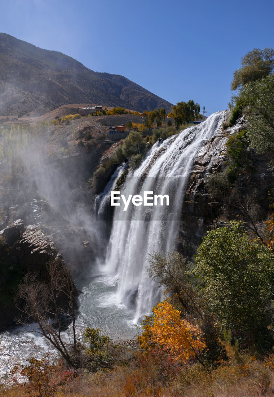 SCENIC VIEW OF WATERFALL AGAINST TREES AND MOUNTAINS