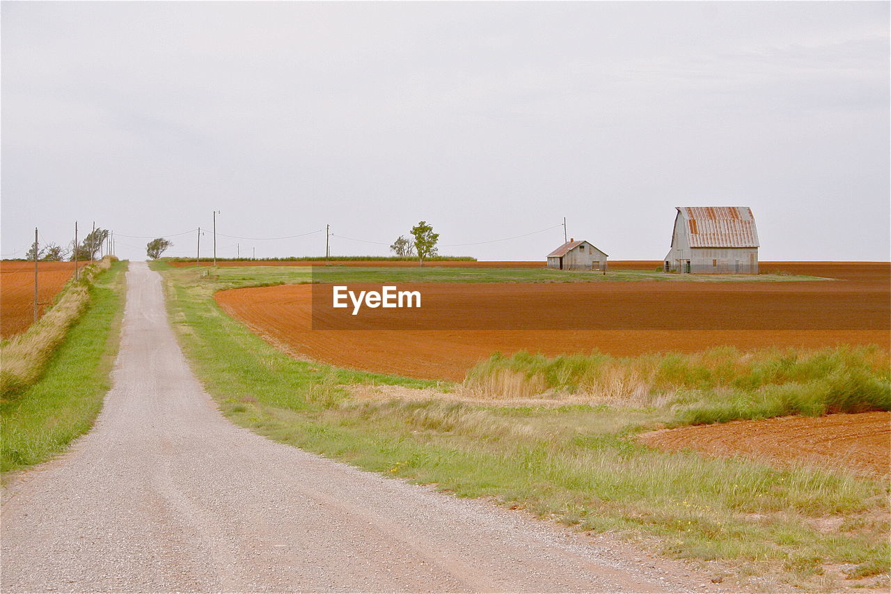 Country road amidst farm against sky