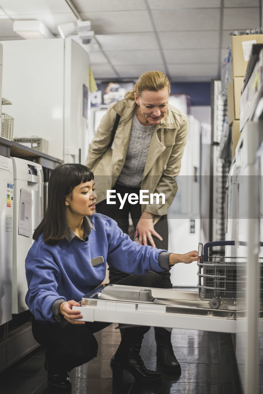 Saleswoman explaining about oven to mature customer in electronics store