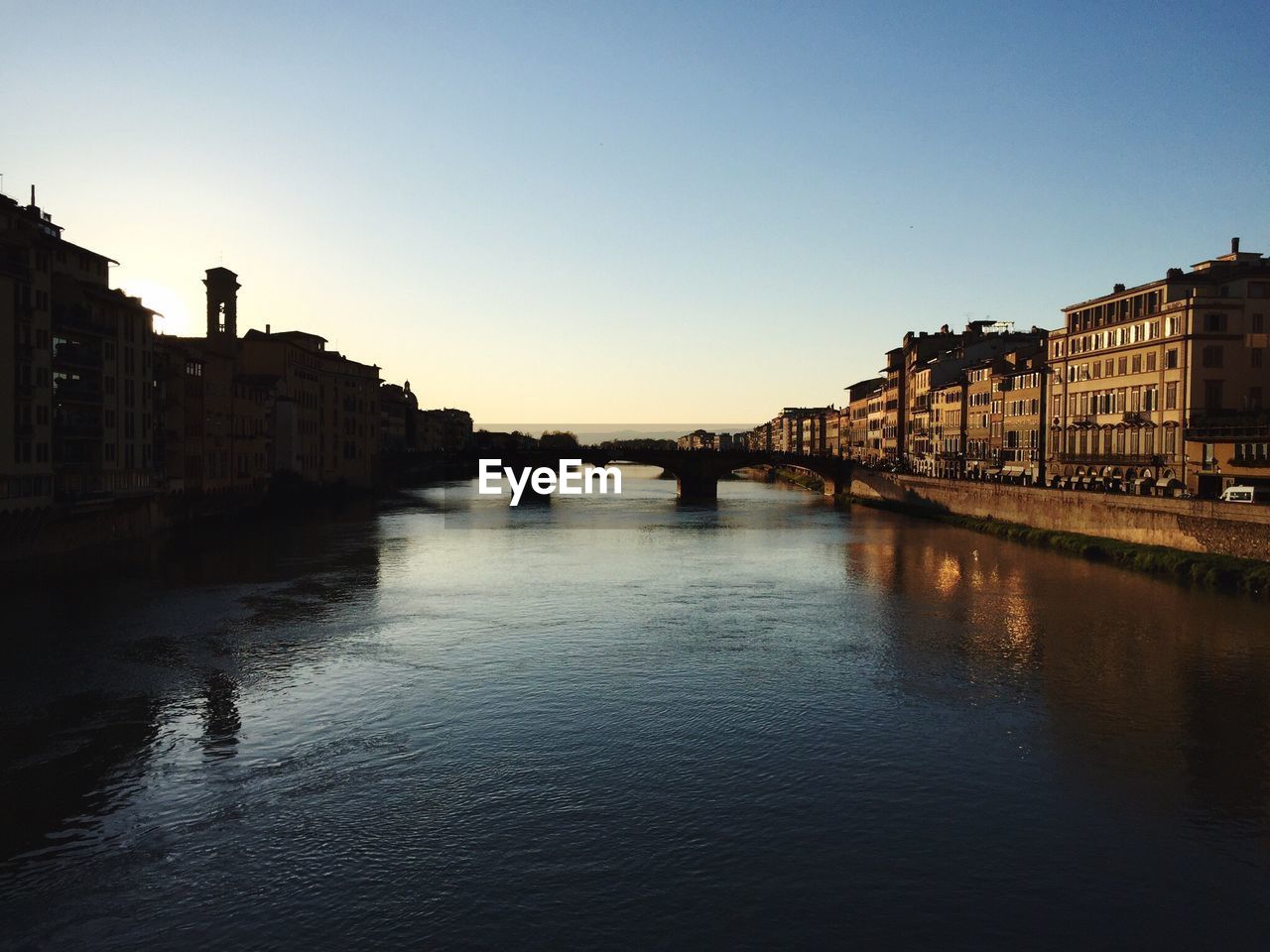 View of buildings by river against clear sky