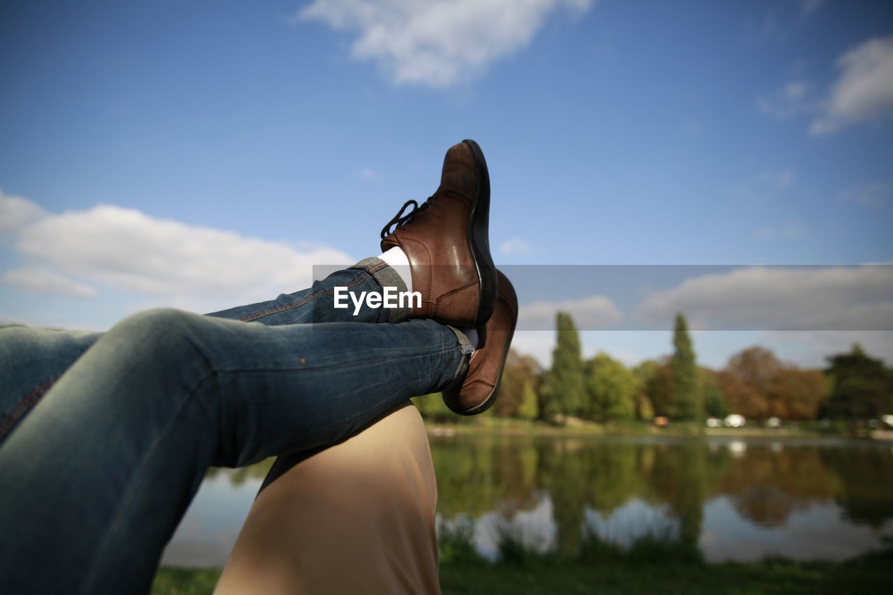 Low section of woman legs on man in park against sky