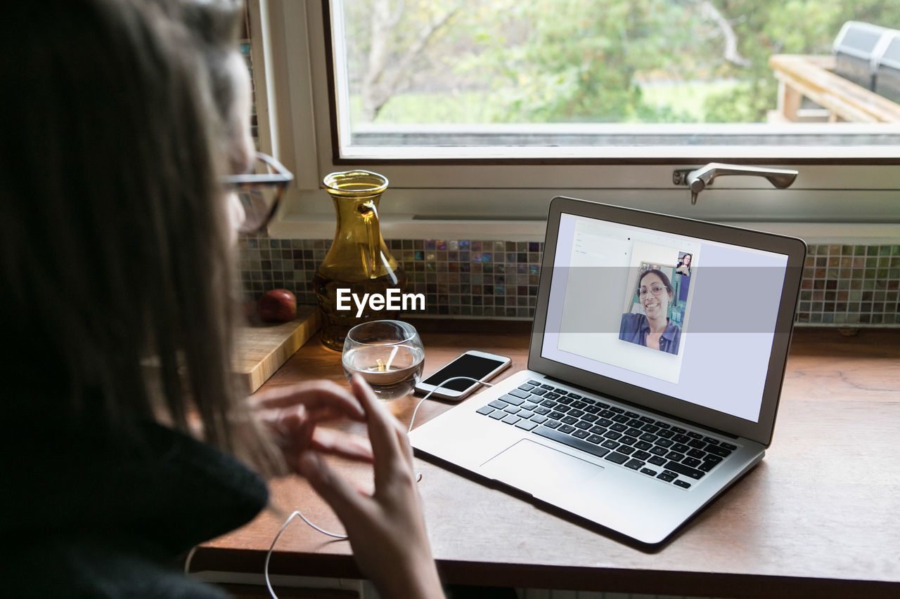 High angle view of businesswoman video calling female colleague on laptop in home office