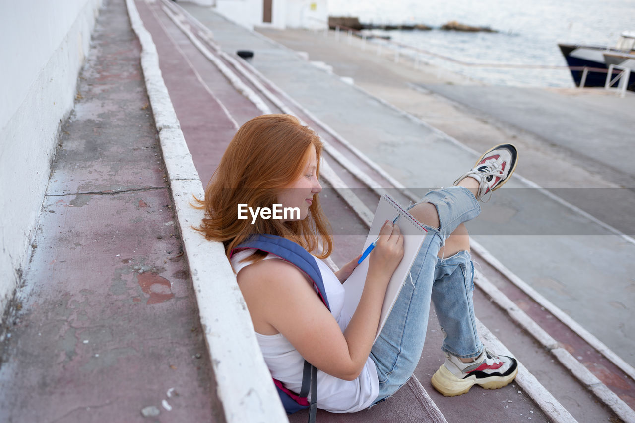 HIGH ANGLE VIEW OF WOMAN USING PHONE WHILE SITTING ON MOBILE