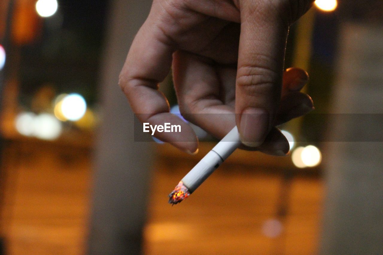 Close-up of hand holding cigarette at night