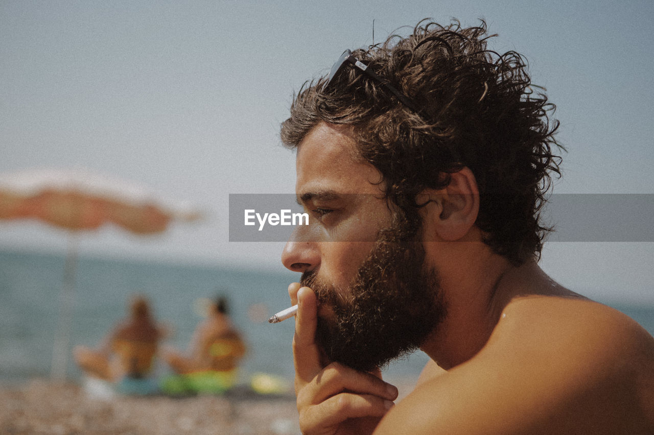 Close-up of shirtless man smoking cigarette at beach