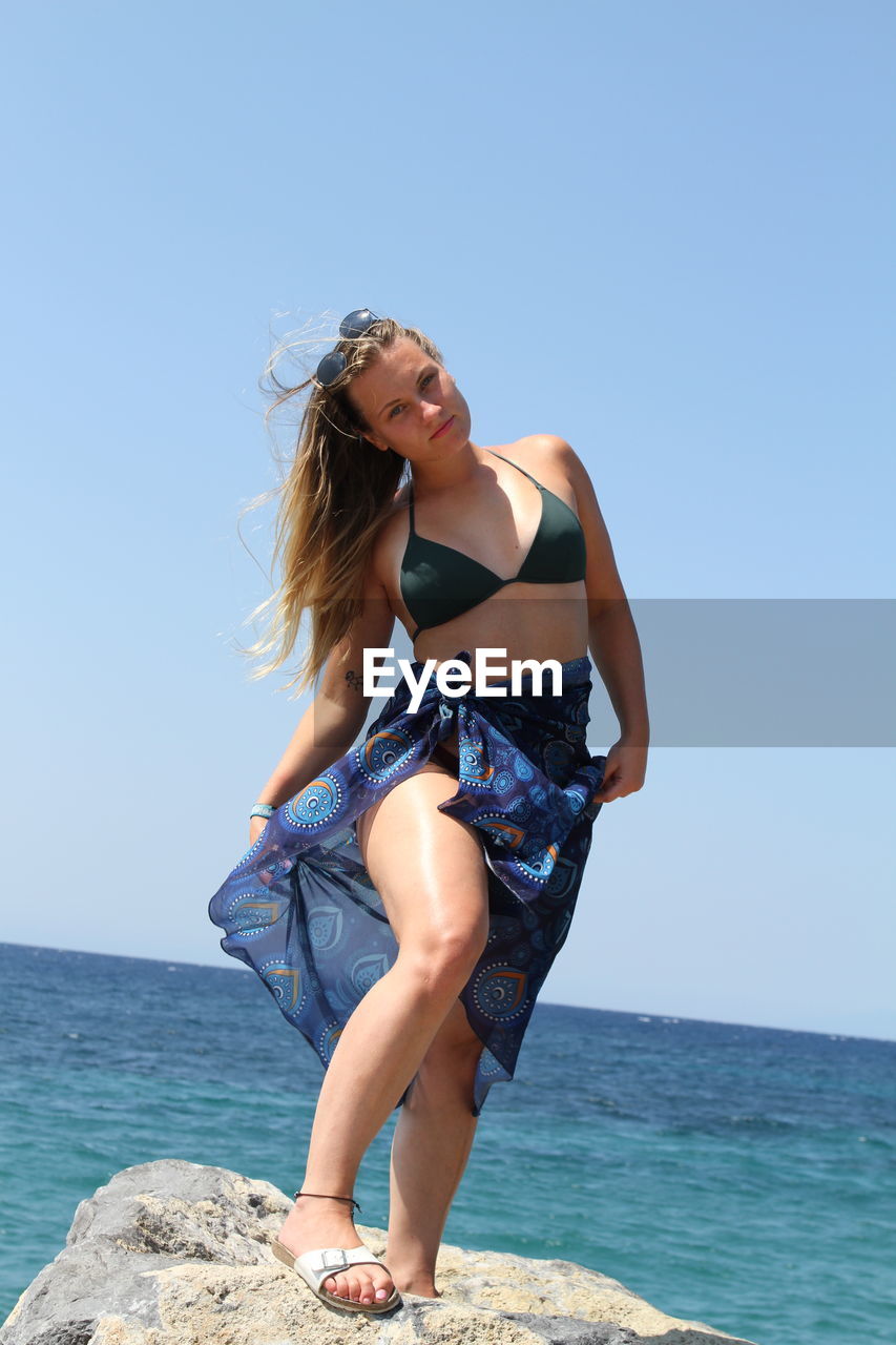 Young woman standing on rock at beach against clear sky