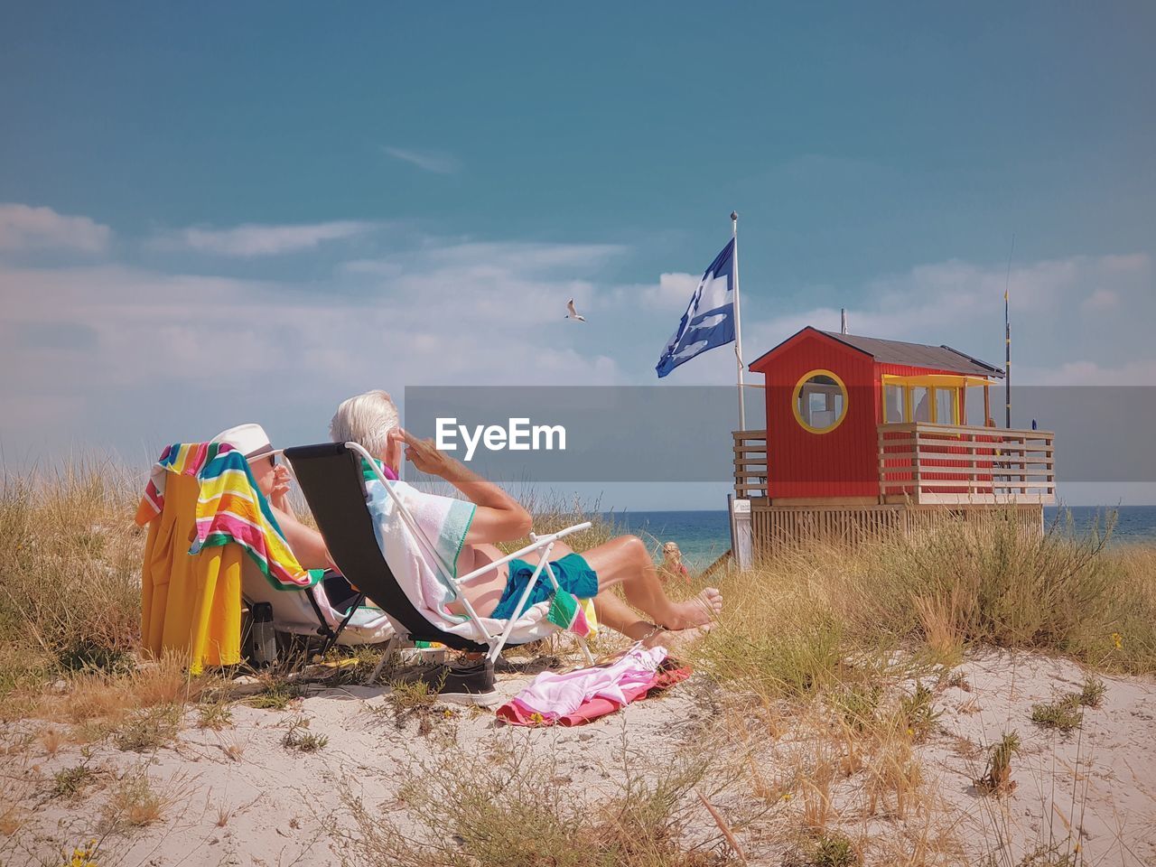 Couple relaxing at beach against sky