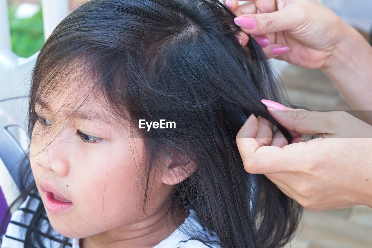 Cropped hands of mother doing daughter hair