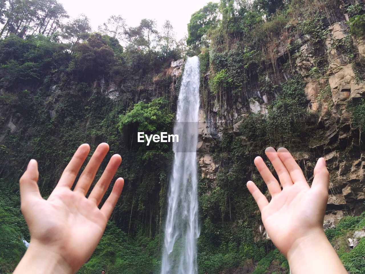 Cropped hands against waterfall in forest