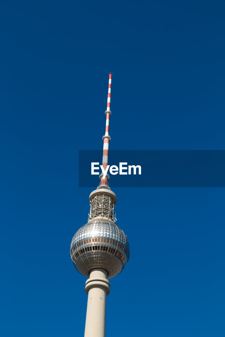 Low angle view of communications tower and buildings against clear blue sky